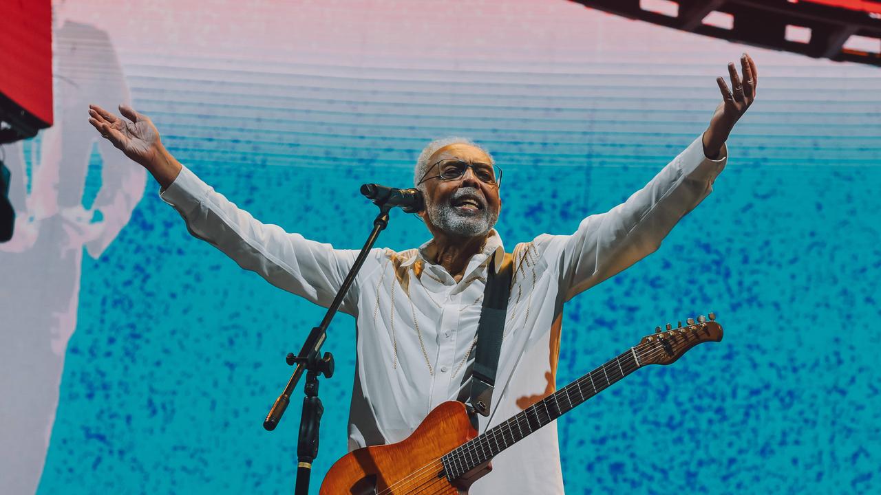 Der brasilianische Musiker Gilberto Gil steht mit einer Gitarre auf der Bühne. Er hält beide Arme in die Höhe und lacht.