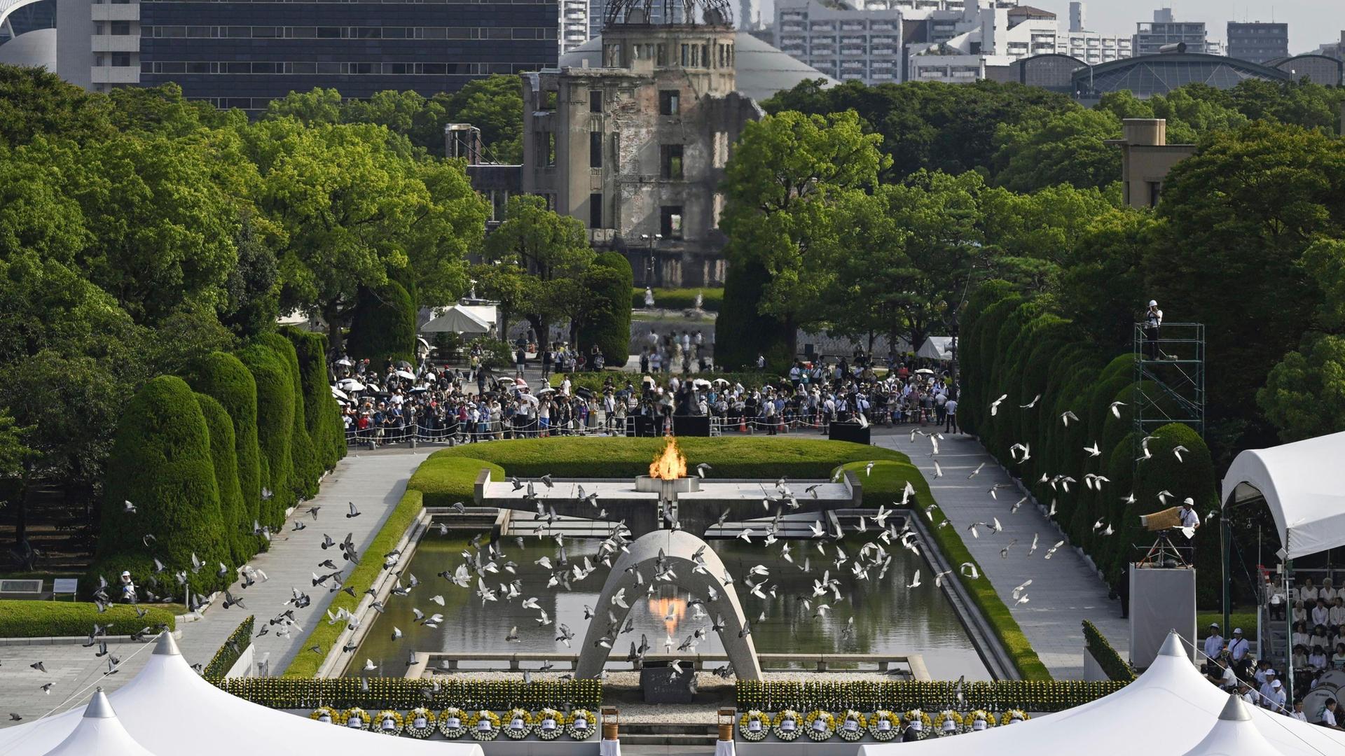 Japan, Hiroshima: Tauben fliegen über den Kenotaph, der den Opfern des Atombombenabwurfs gewidmet ist, während der jährlichen Zeremonie zum 79. Jahrestag des ersten Atombombenabwurfs im Peace Memorial Park. 