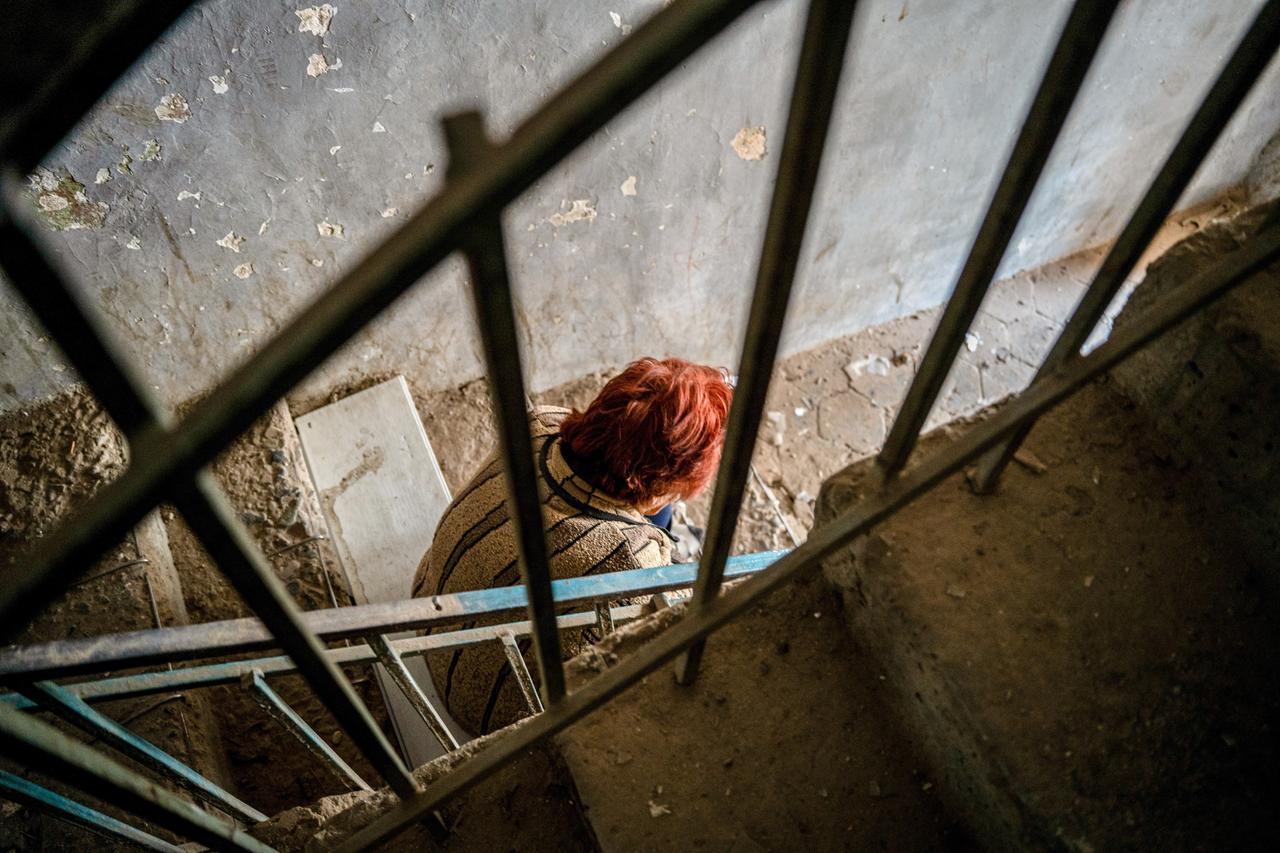 Eine Frau sitzt auf einer Treppe in einem Wohngebäude, das bei einem aserbaidschanischen Angriff auf Stepanakert zerstört wurde. Um sie herum sind Trümmer.