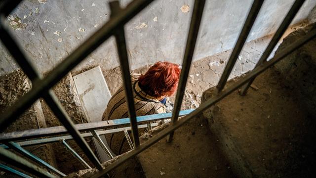 Eine Frau sitzt auf einer Treppe in einem Wohngebäude, das bei einem aserbaidschanischen Angriff auf Stepanakert zerstört wurde. Um sie herum sind Trümmer.