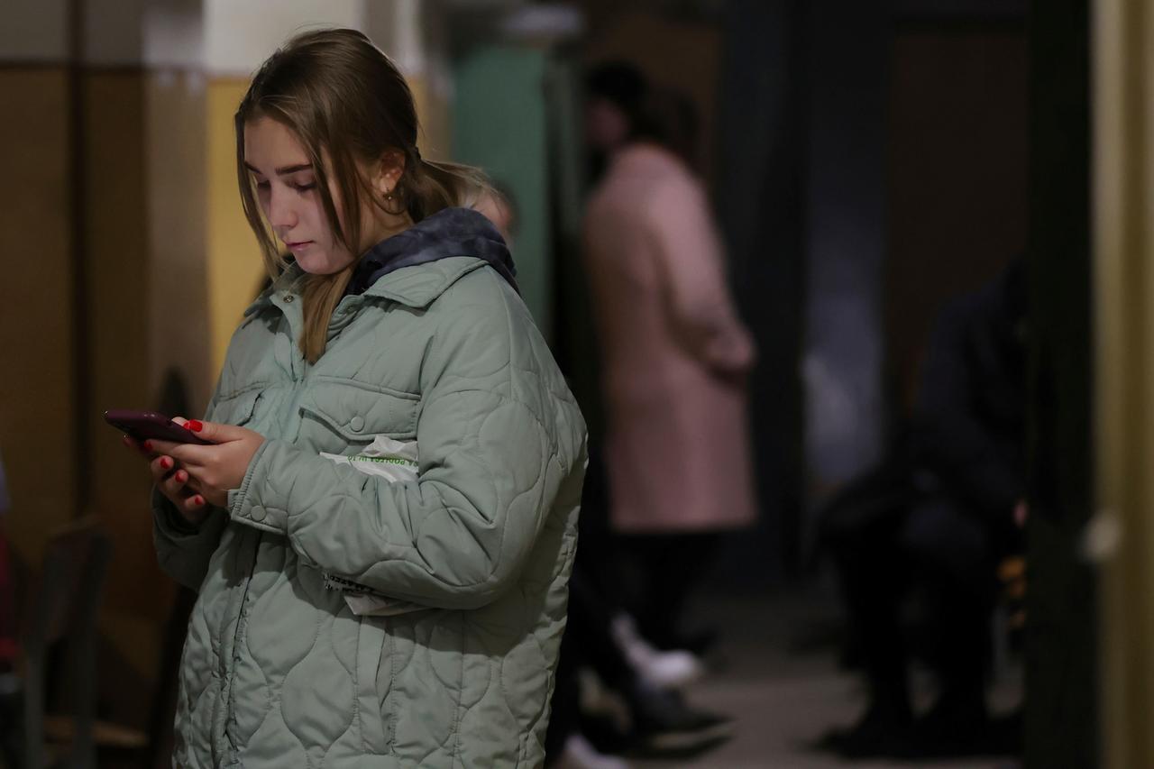 Eine junge Frau steht in einem Schutzbunker in Liviv, Ukraine. und schaut auf ihr Smartphone.
