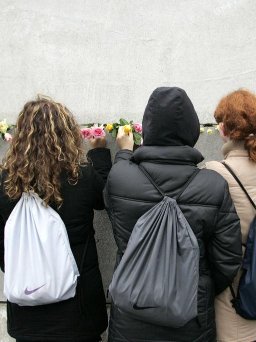 Junge Frauen stecken Blumen in eine Mauerritze Junge Frauen stecken Blumen in eine Mauerritze