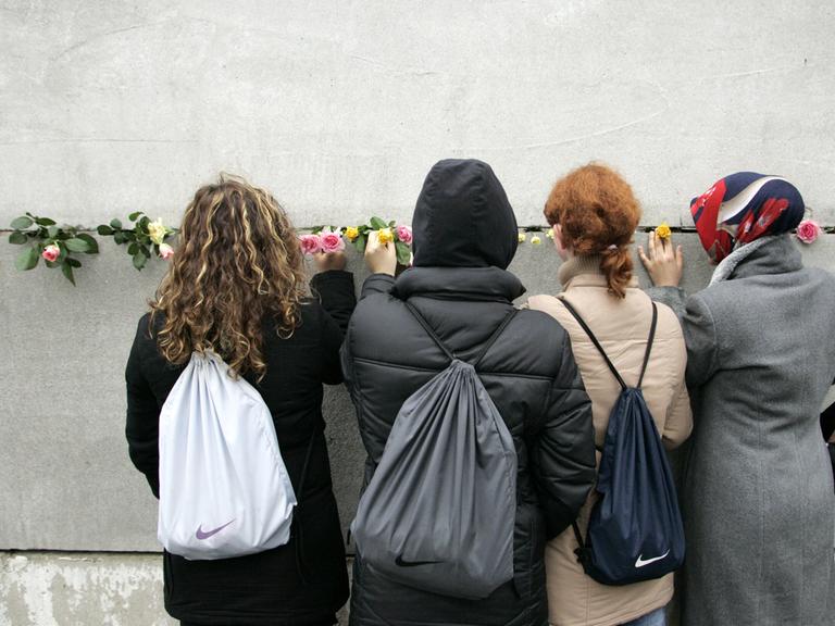 Junge Frauen stecken Blumen in eine Mauerritze Junge Frauen stecken Blumen in eine Mauerritze