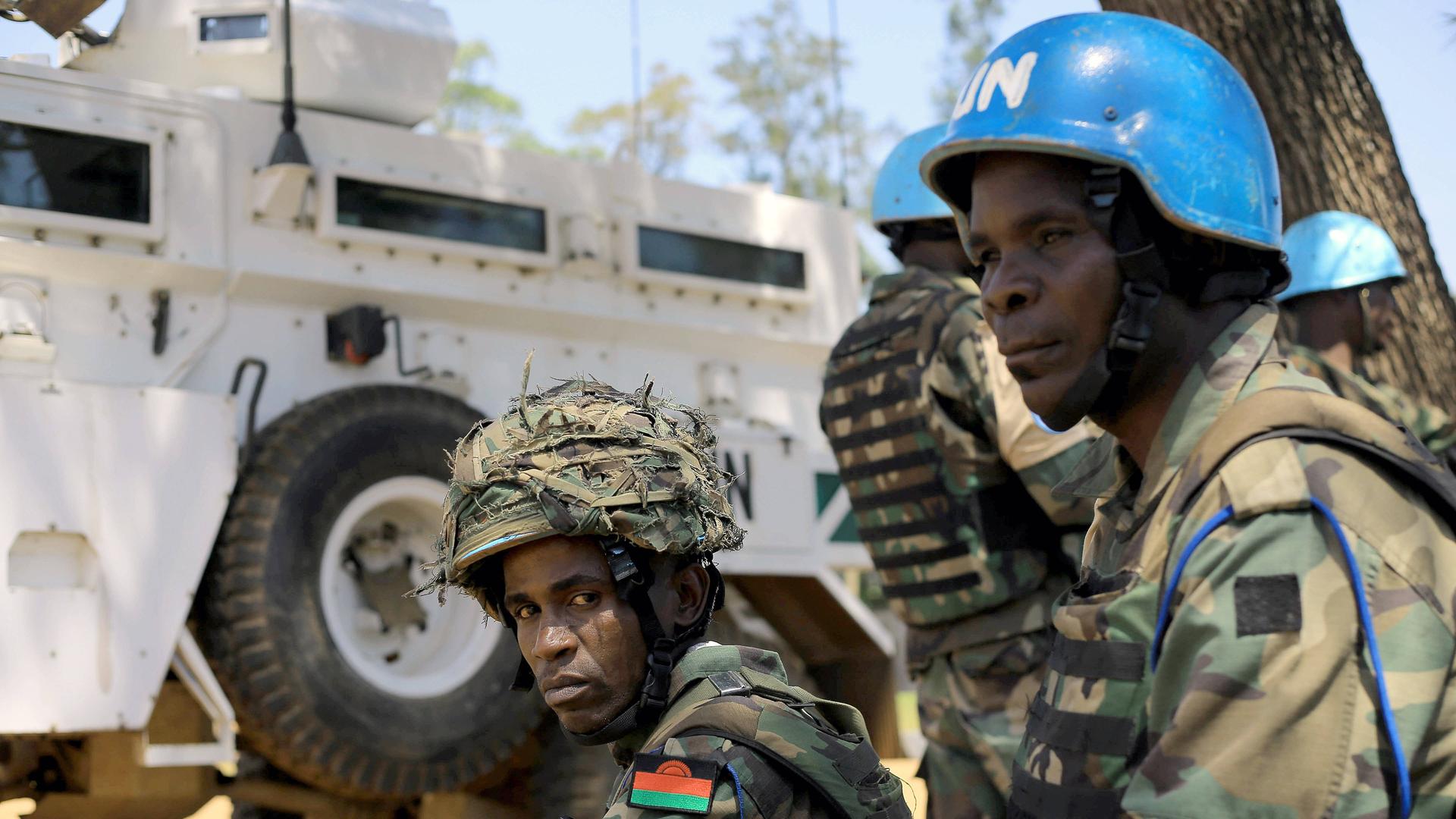 Zwei Soldaten mit Helmen sitzt zwischen militärischen Fahrzeugen der UN.