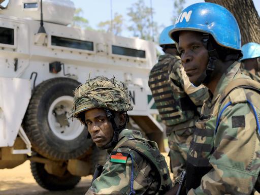 Zwei Soldaten mit Helmen sitzt zwischen militärischen Fahrzeugen der UN.