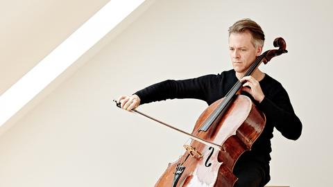 Alban Gerhardt sitzt in einem lichtdurchfluteten Raum und spielt sein Instrument.