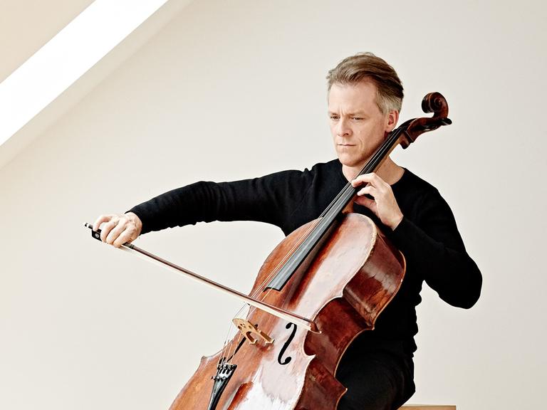 Alban Gerhardt sitzt in einem lichtdurchfluteten Raum und spielt sein Instrument.