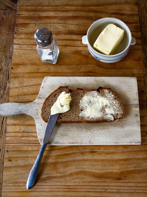 Salz, Butter und Brot auf einem Brettchen. 