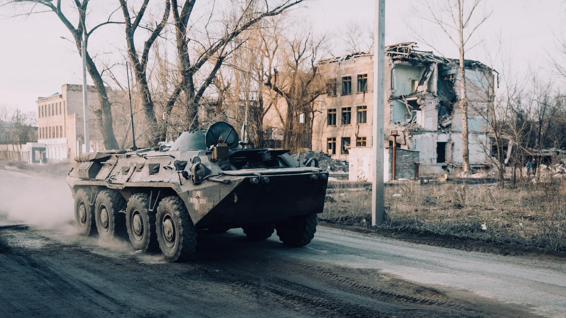 Ein Panzer steht vor einem zerstörten Gebäude.