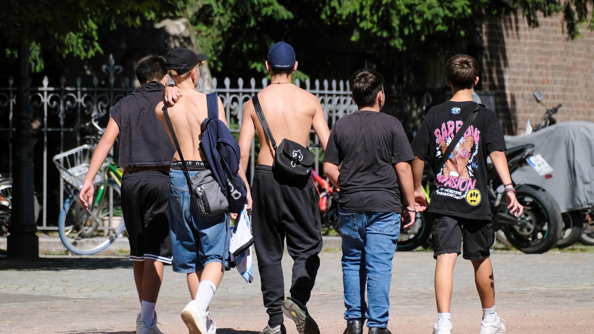 Fünf Jugendliche auf dem Schulweg in Düsseldorf. Sie tragen lockere, bunt bedruckte Kleidung. Zwei Jungen sind oberkörperfrei unterwegs.
