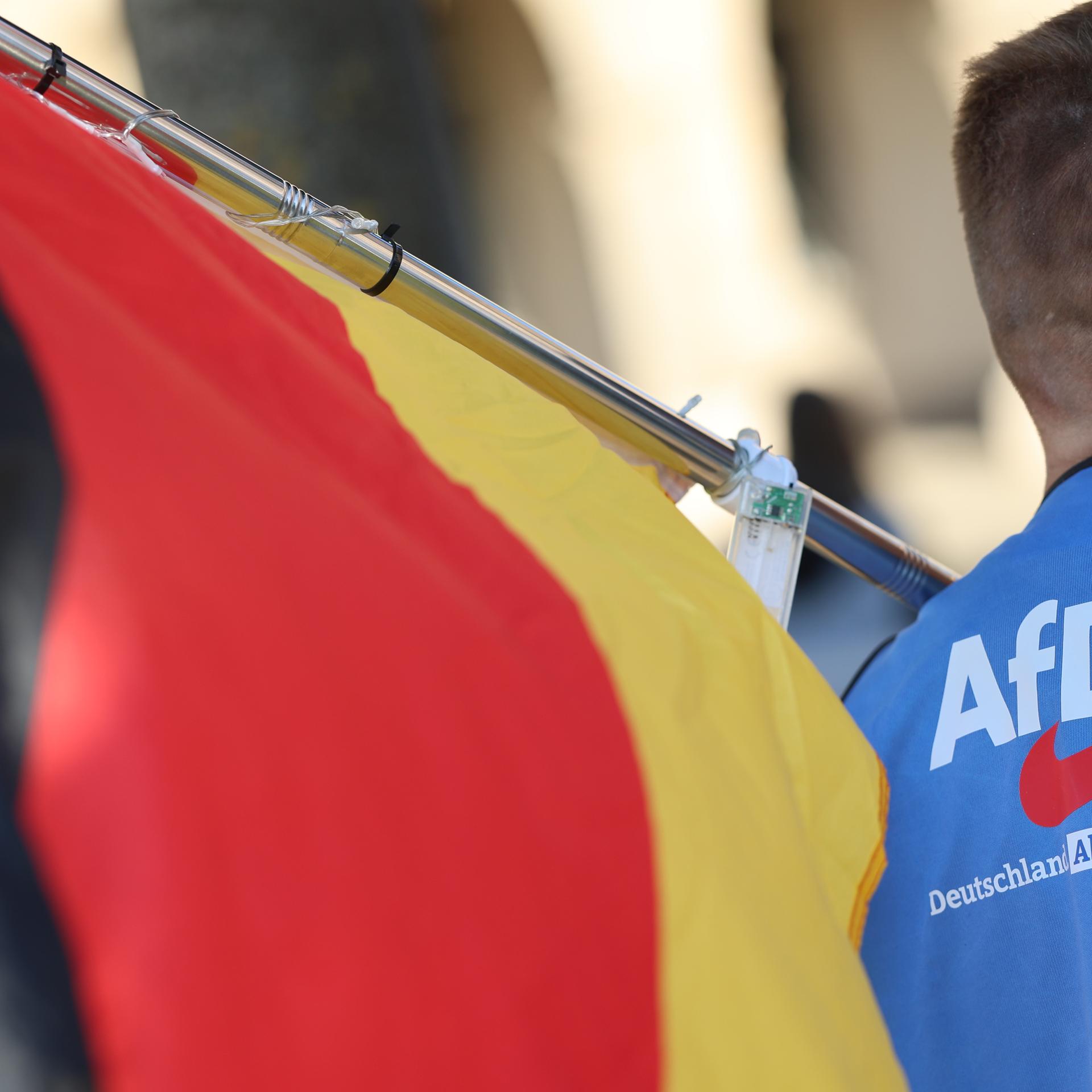 ARCHIV - 12.05.2025, Sachsen-Anhalt, Halberstadt: Ein Teilnehmer der Montagsdemonstration trägt eine gelbe Warnweste mit einem AfD-Logo und der Aufschrift "Deutschland. Aber normal." und hält eine Deutschlandfahne.