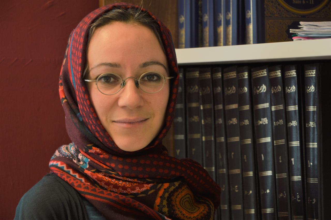 Porträt der islamischen Theologin Muna Tatari vor einer Bücherwand. 