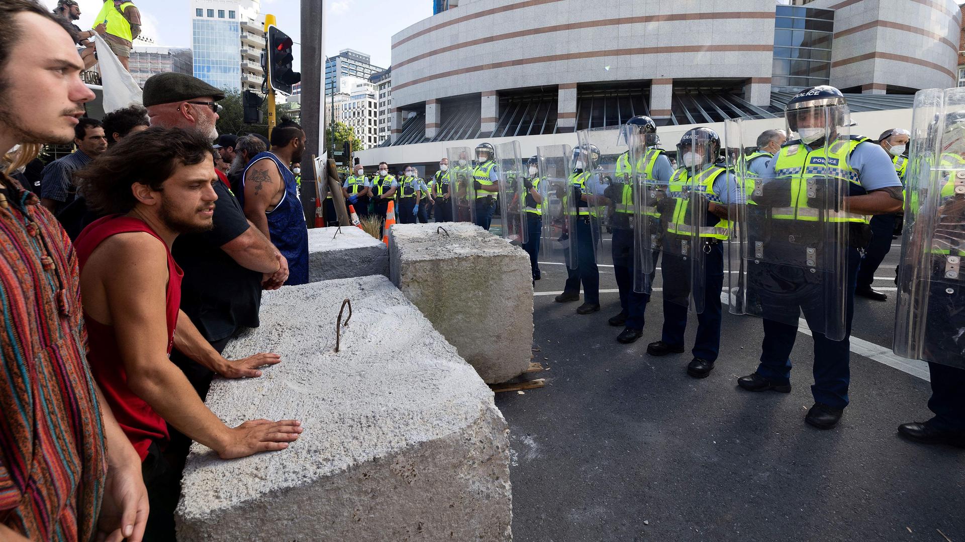 Polizisten stehen Corona-Impfgegnern gegenüber, die hinter großen Steinblöcken stehen.