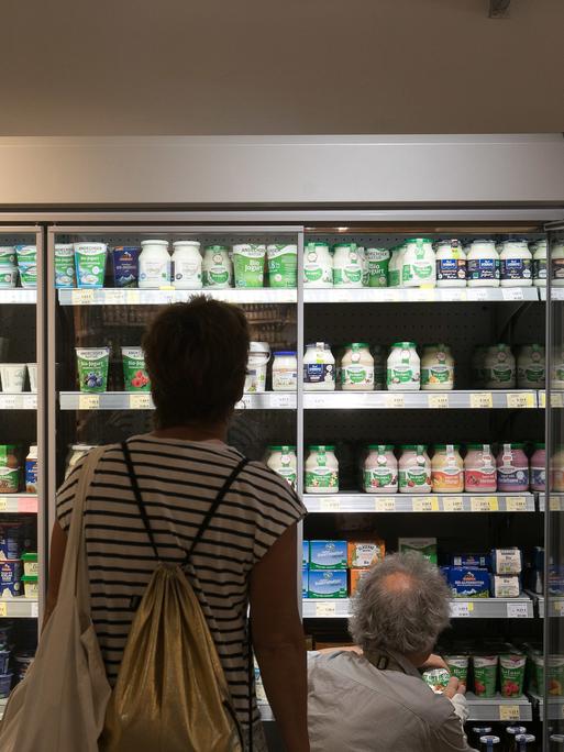 Ein Kühlregal für Milchprodukte vor dem zwei Personen von hinten zu sehen sind. 