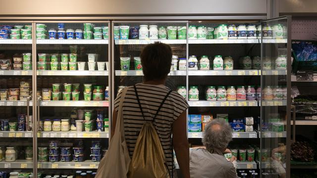 Ein Kühlregal für Milchprodukte vor dem zwei Personen von hinten zu sehen sind. 