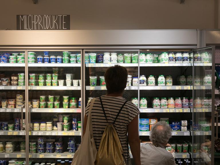 Ein Kühlregal für Milchprodukte vor dem zwei Personen von hinten zu sehen sind. 