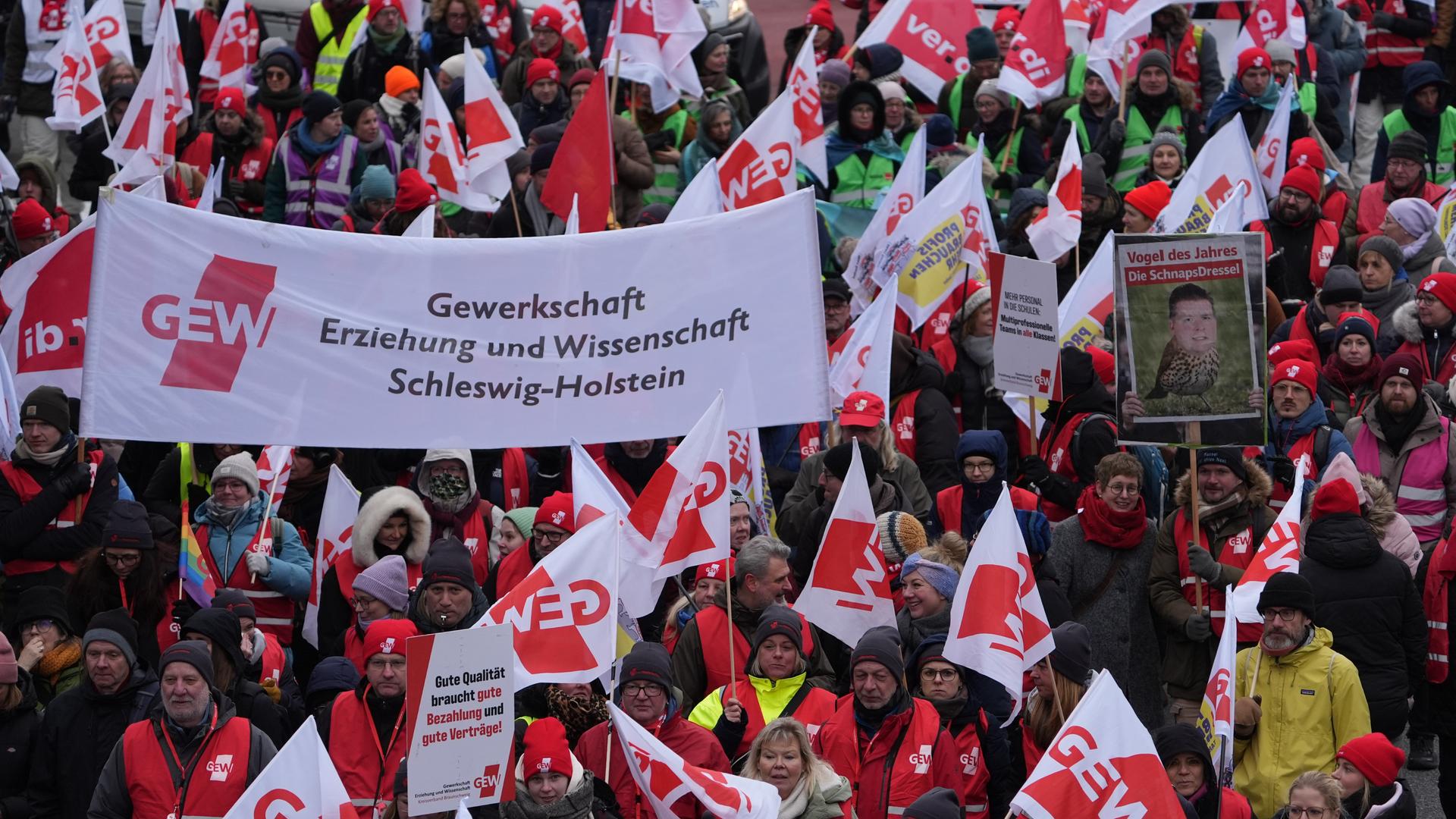 Viele Menschen laufen über eine Straße, sie tragen Fahnen und rot-weiße Banner mit der Aufschrift "GEW".