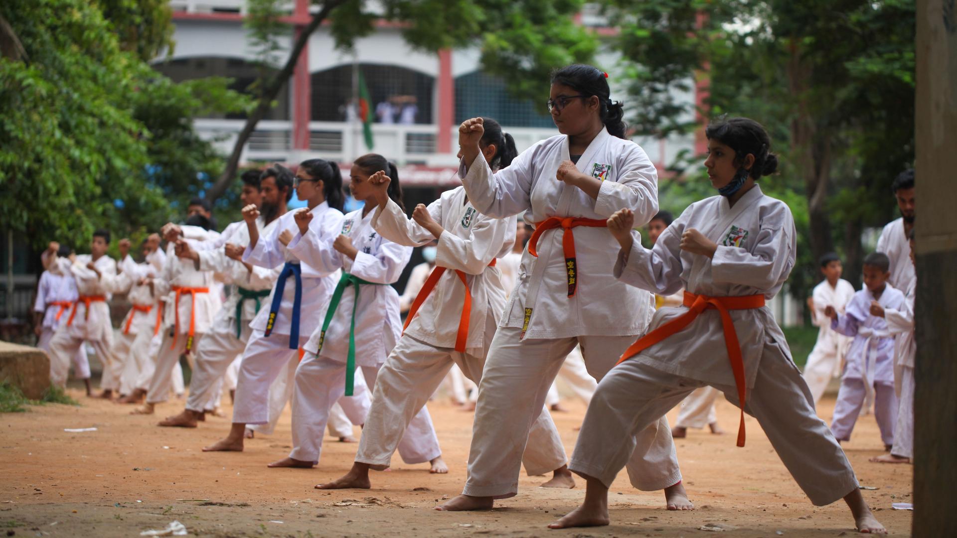 Das Bild zeigt Mädchen aus Bangladesch, die draußen in weißen Karateanzügen und unterschiedlichen Gürtelfarben Karate trainieren.