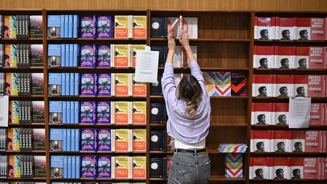 Das Foto zeigt ein Bücher-Regal und davor eine Frau.
