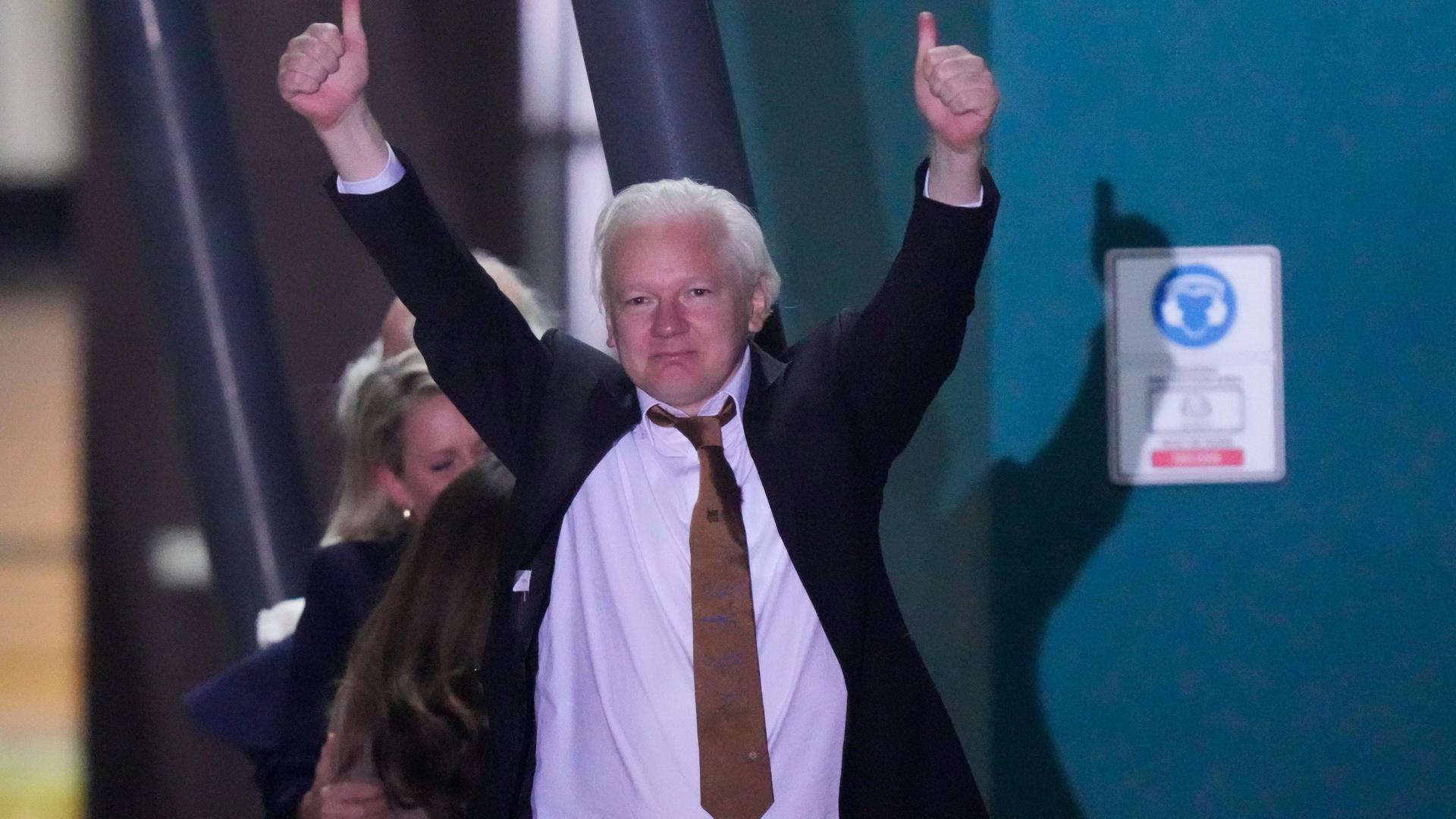Julian Assange steigt in Australien aus dem Flugzeug. Er hält beide Arme hoch. 