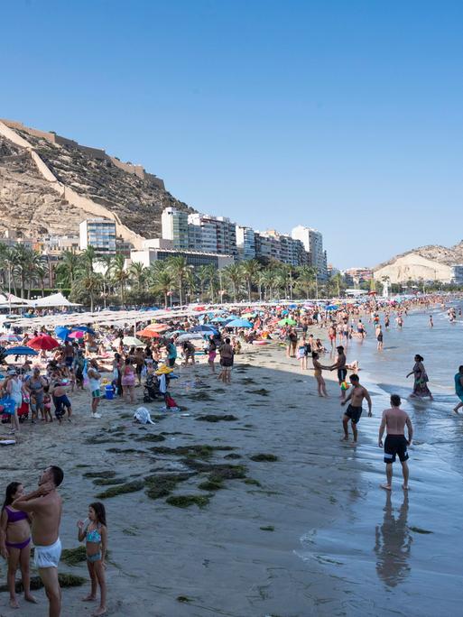 Menschen am Strand in Alicante, im Hintergrund dichte Bebauung.