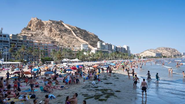 Menschen am Strand in Alicante, im Hintergrund dichte Bebauung.