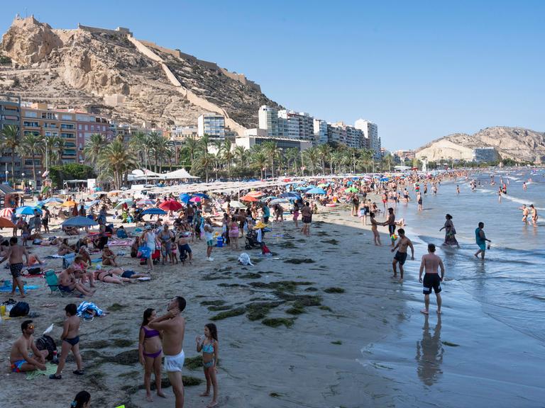 Menschen am Strand in Alicante, im Hintergrund dichte Bebauung.