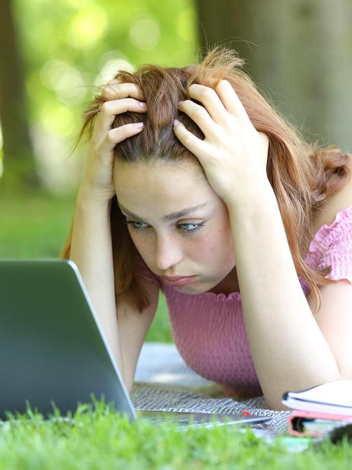 Ein Mädchen schaut auf ihr Laptop und rauft sich in den Haaren. Ein Mädchen schaut auf ihr Laptop und rauft sich in den Haaren.