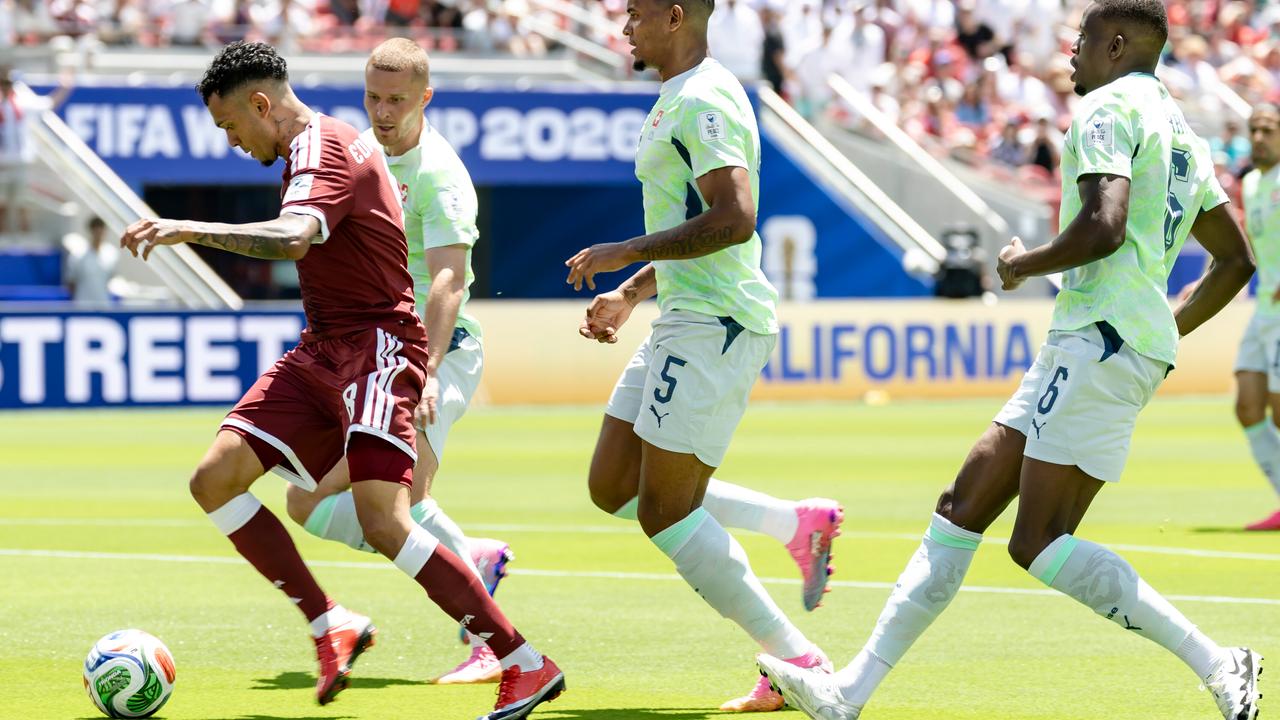 Vier Fußballspieler rennen um den Ball, einer trägt ein dunkelrotes Trikot, die anderen hellgrüne.