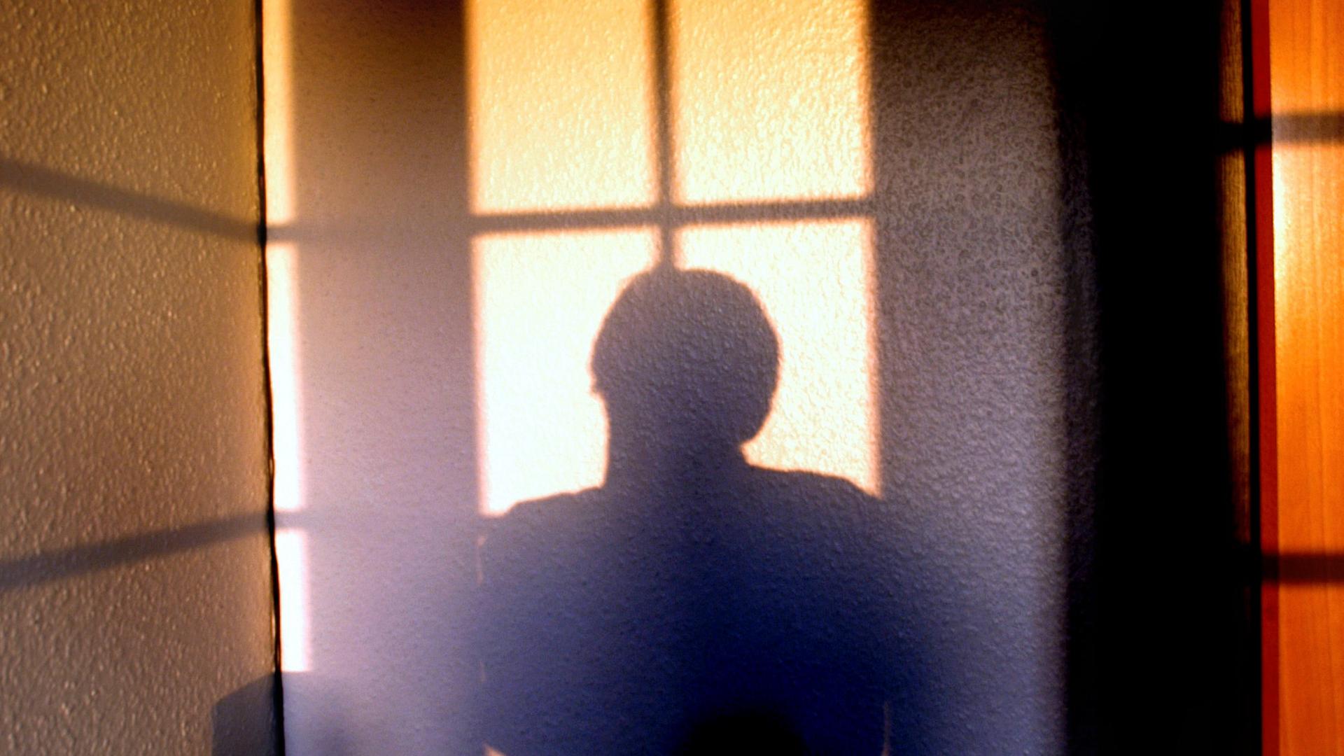 Die Silhouette einer Person hebt sich von einer hellen Wand ab. Die Silhouette einer Person hebt sich von einer hellen Wand ab.