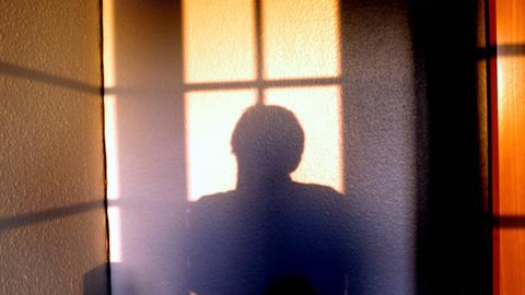 Die Silhouette einer Person hebt sich von einer hellen Wand ab. Die Silhouette einer Person hebt sich von einer hellen Wand ab.
