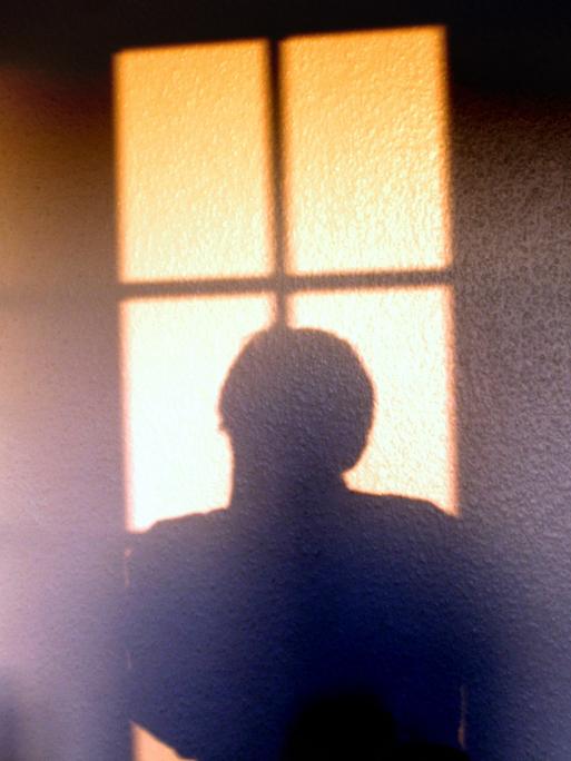 Die Silhouette einer Person hebt sich von einer hellen Wand ab.