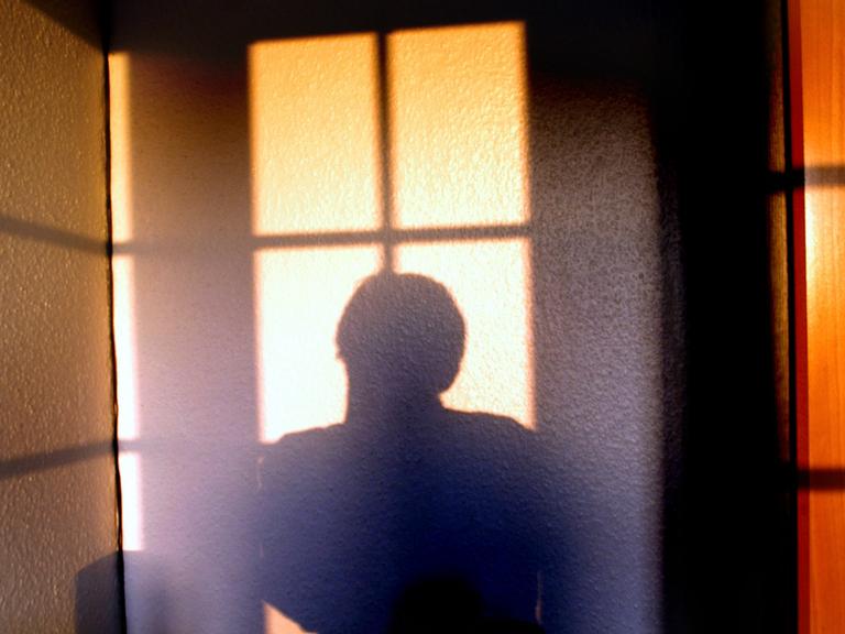 Die Silhouette einer Person hebt sich von einer hellen Wand ab.