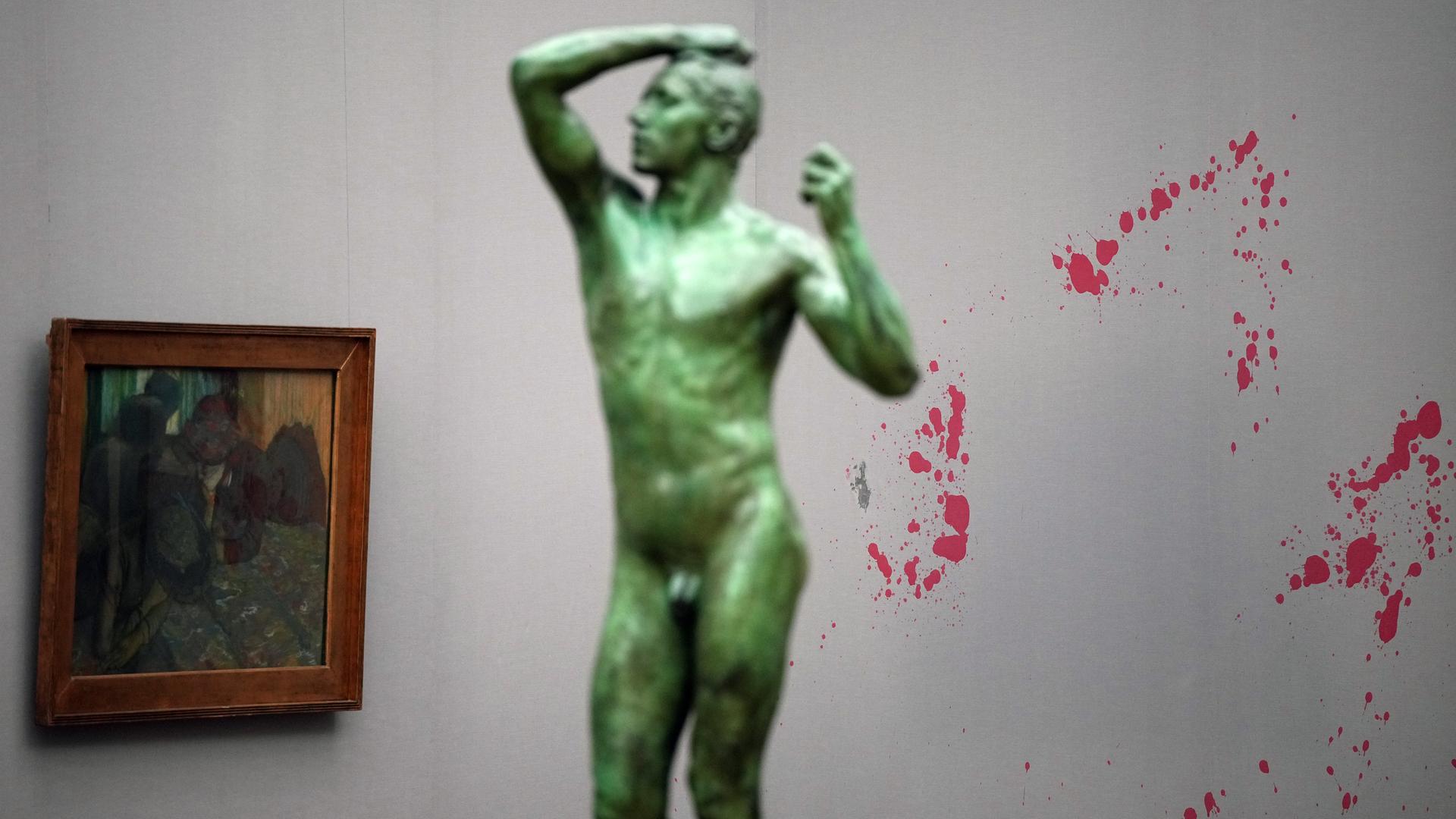 Rote Flecken sind im Impressionistensaal der Alten Nationalgalerie an einer Wand zu sehen. Im Vordergrund steht die Statue "The Bronze Age" von Auguste Rodin, links hängt das Gemälde "Unterhaltung" von Edgar Degas. 