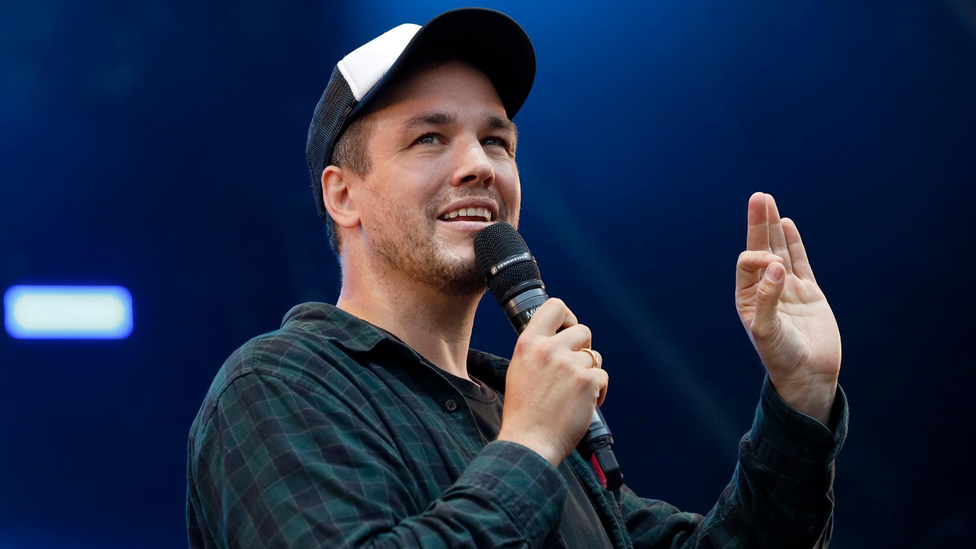 Comedian und Synchronsprecher Jan van Weyde, auf einer Bühne mit Mikrofon in der Hand.