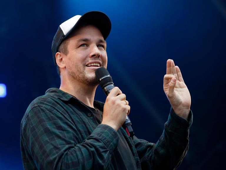 Comedian und Synchronsprecher Jan van Weyde, auf einer Bühne mit Mikrofon in der Hand.