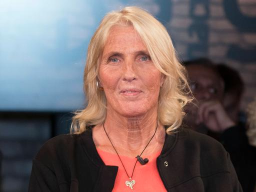 Heike Rath sitzt im Fernsehstudio. Sie hat schulterlanges blondes Haar und trägt eine Halskette mit einem silbernen Elefantenkopf.