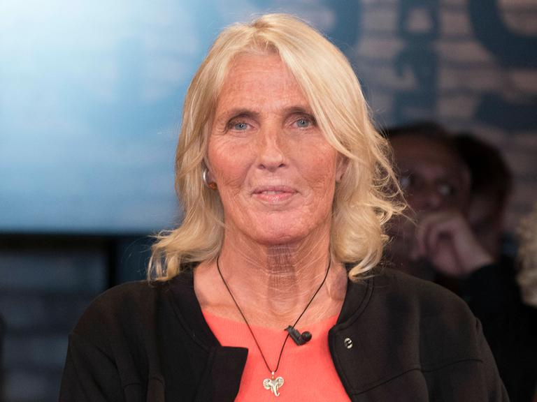 Heike Rath sitzt im Fernsehstudio. Sie hat schulterlanges blondes Haar und trägt eine Halskette mit einem silbernen Elefantenkopf.