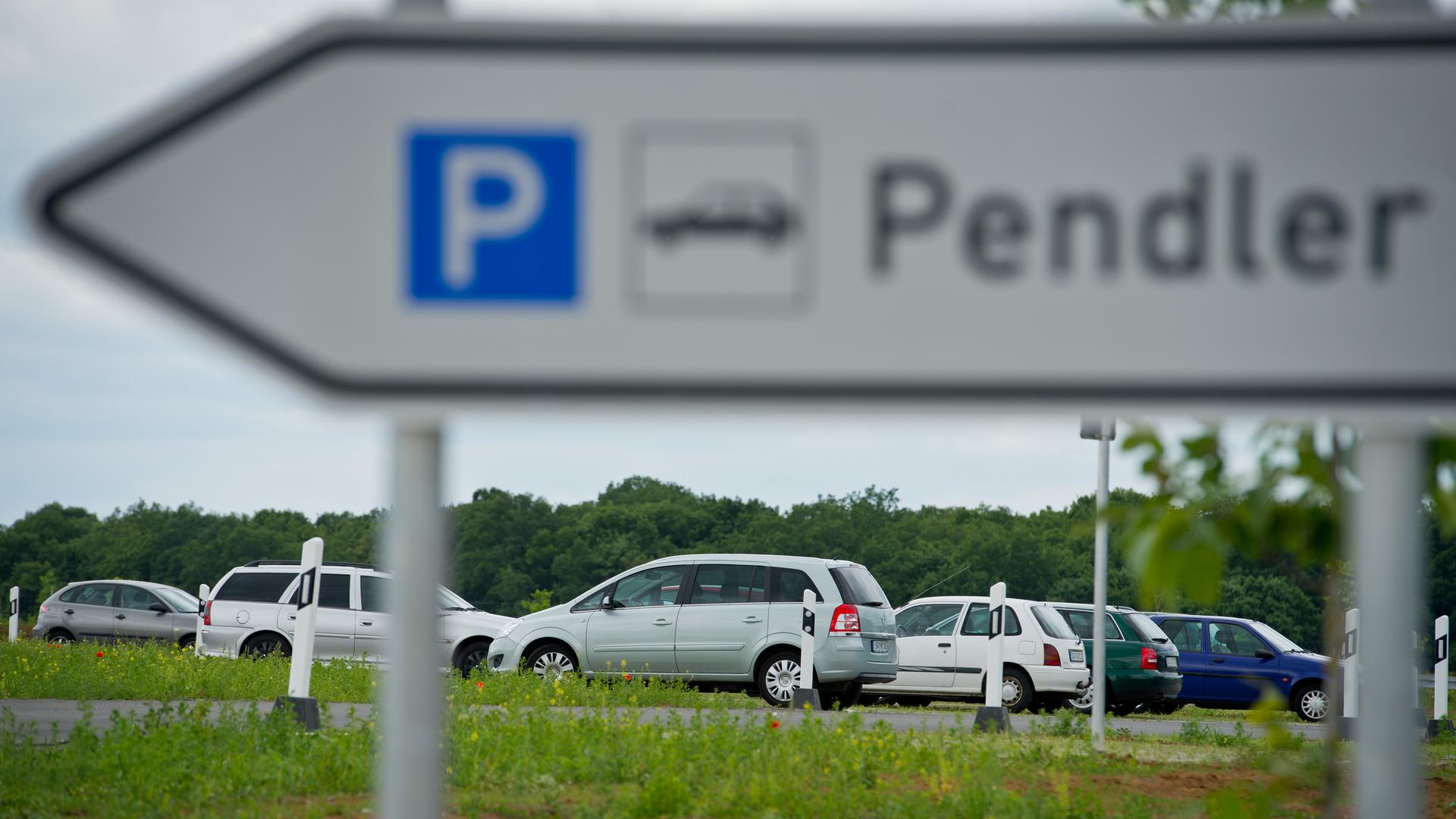 Ds Schild "Pendler" sieht man unscharf im Vordergrund. Darunter scharf im Hintergrund mehrere Autos. 