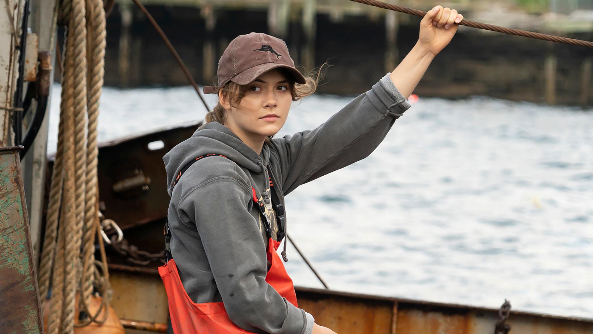 Schauspielerin Emilia Jones sitzt in einer Szene des oscarprämierten Films "Coda" in Arbeitskleidung einem Fischerboot und schaut in die Kamera.