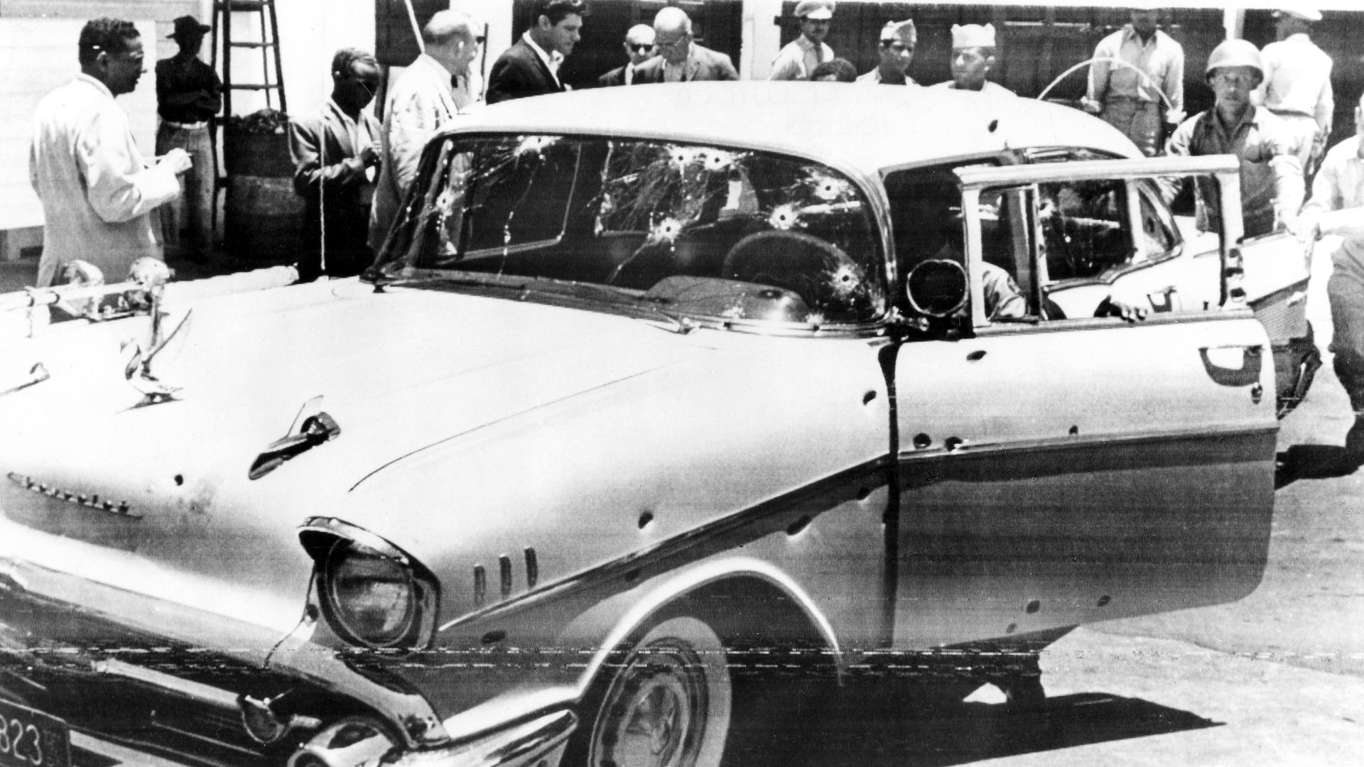 Die Schwarz-Weiß-Aufnahme zeigt das Auto von Rafael Trujillo. Die Autoform ähnelt amerikanischen Limousinen aus den 60ern. Etliche Einschusslöcher legen nahe, dass Trujillo in dem Auto gestorben ist.