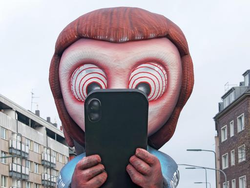 Mottowagen beim Düsseldorfer Rosenmontagszug: Ein aus Pappmaché gebautes Kind schaut gebannt auf ein Smartphone. In den Augen des Kindes sind Hypnose-Ringe zu sehen. Mottowagen beim Düsseldorfer Rosenmontagszug: Ein aus Pappmaché gebautes Kind schaut gebannt auf ein Smartphone. In den Augen des Kindes sind Hypnose-Ringe zu sehen.