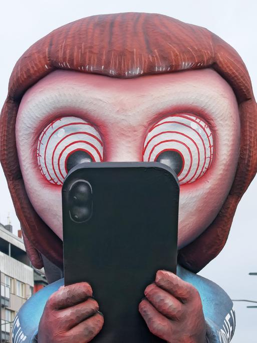 Mottowagen beim Düsseldorfer Rosenmontagszug: Ein aus Pappmaché gebautes Kind schaut gebannt auf ein Smartphone. In den Augen des Kindes sind Hypnose-Ringe zu sehen. 