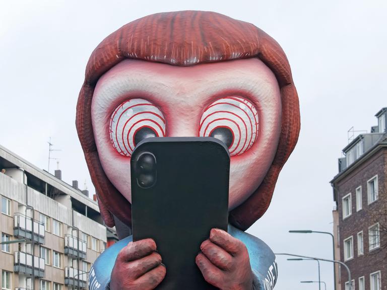Mottowagen beim Düsseldorfer Rosenmontagszug: Ein aus Pappmaché gebautes Kind schaut gebannt auf ein Smartphone. In den Augen des Kindes sind Hypnose-Ringe zu sehen. 