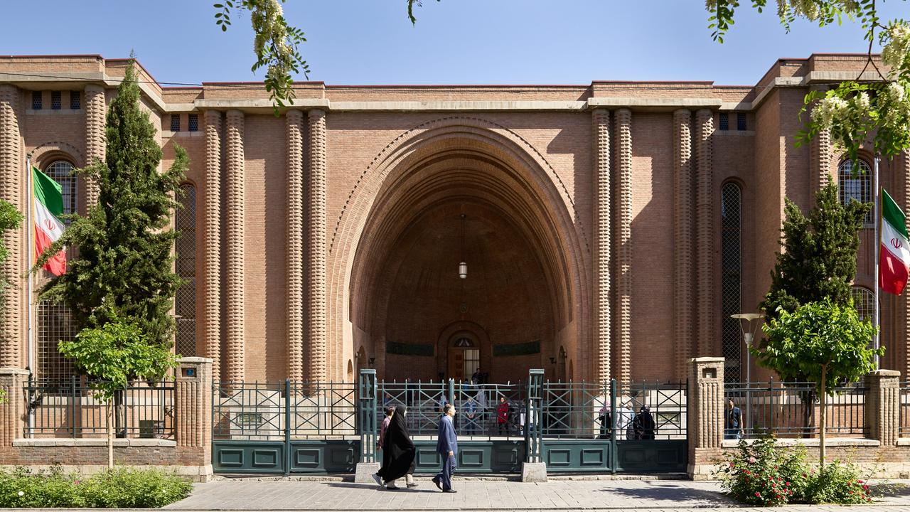 Das Nationalmuseum von dem Iran in der Hauptstadt Teheran. Ein Haus mit einem riesigen Torbogen. Davor ist ein Zaun.