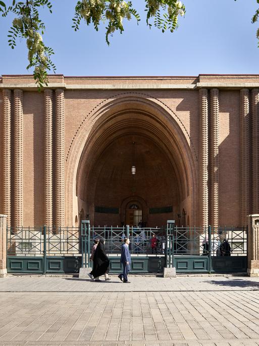 Das Nationalmuseum von dem Iran in der Hauptstadt Teheran. Ein Haus mit einem riesigen Torbogen. Davor ist ein Zaun.