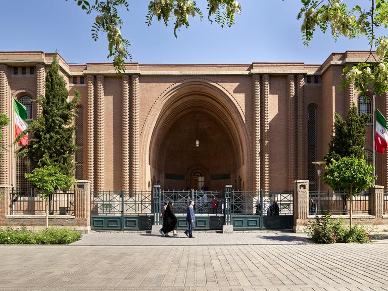 Das Nationalmuseum von dem Iran in der Hauptstadt Teheran. Ein Haus mit einem riesigen Torbogen. Davor ist ein Zaun.