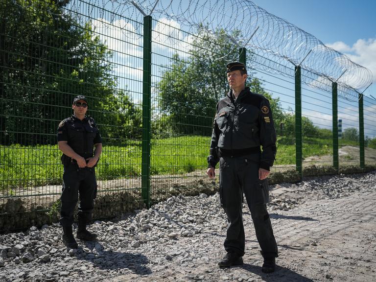 Zwei finnische Grenzbeamte stehen vor dem finnisch-russischen Grenzzaun.