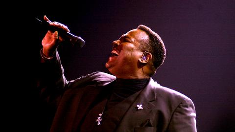 Luther Vandross trägt ein schwarzes Rollkragenshirt und einen dunklen Anzug und singt 2002 auf der Bühne der Sheffield Arena aus voller Brust in ein Mikrofon
