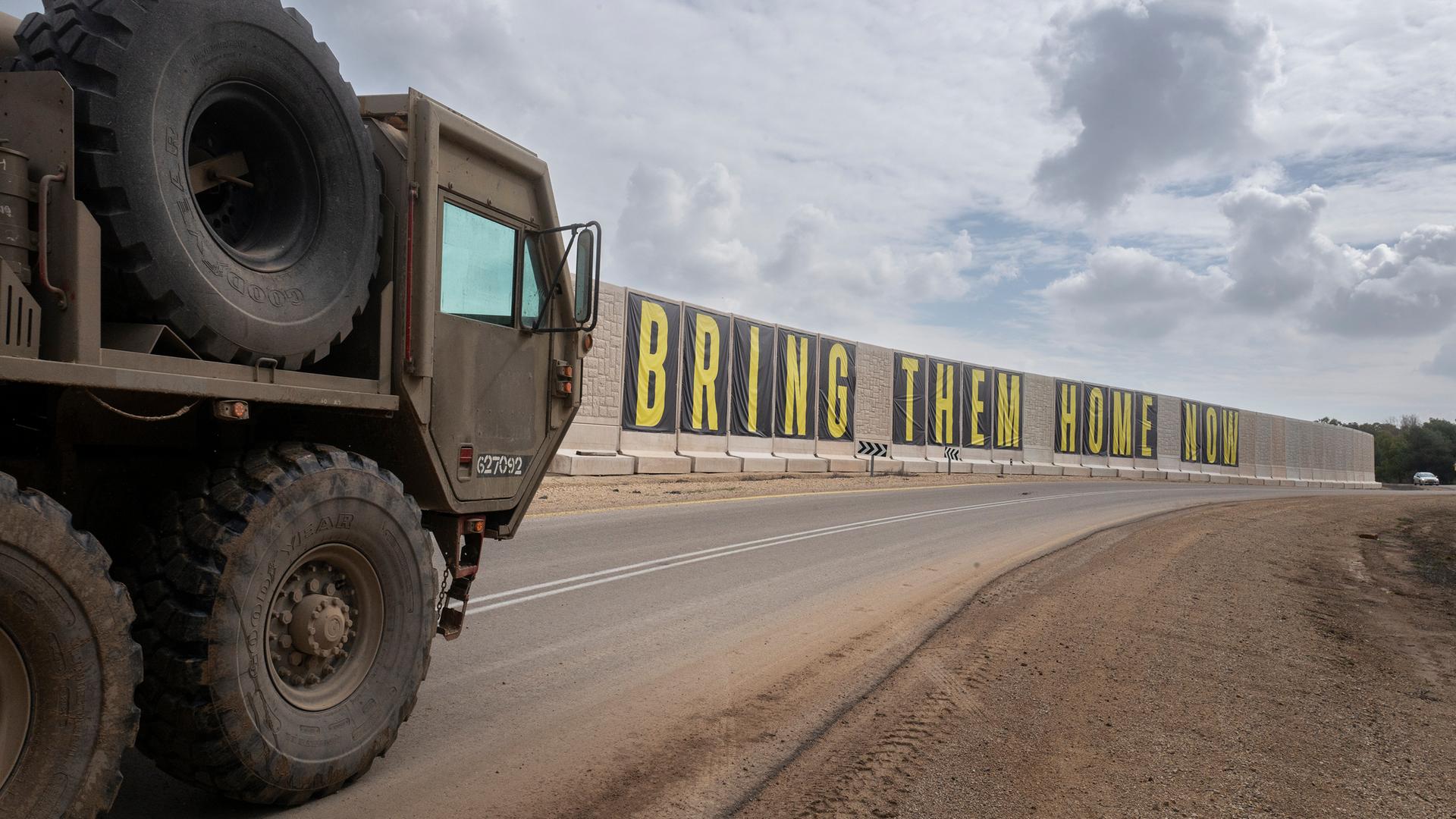 Ein israelisches Militärfahrzeug fährt an einer Wand vorbei, auf dem geschrieben steht: "Bring Them Home Now" ("Holt sie jetzt nach Hause").